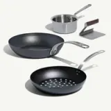 A set of cooking pans and utensils includes a skillet, a perforated frying pan, and a small saucepan with a handle.