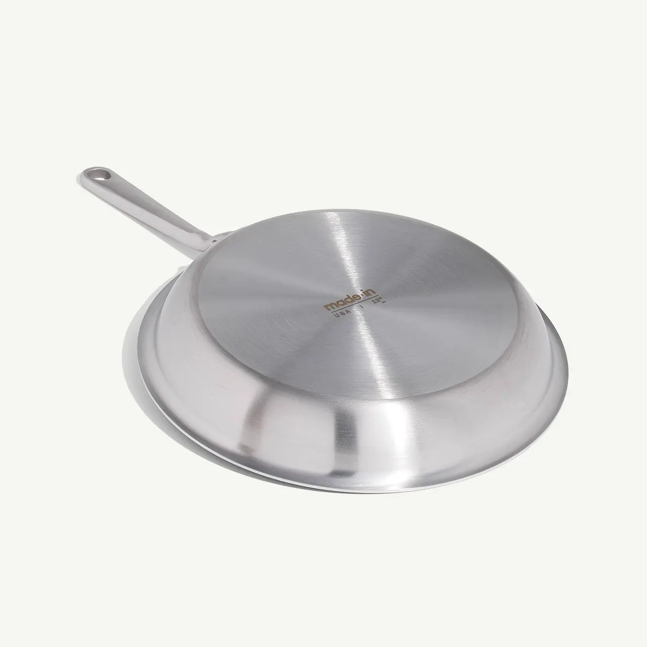 A stainless steel frying pan with a long handle and a flat, fitted lid, set on a light background.