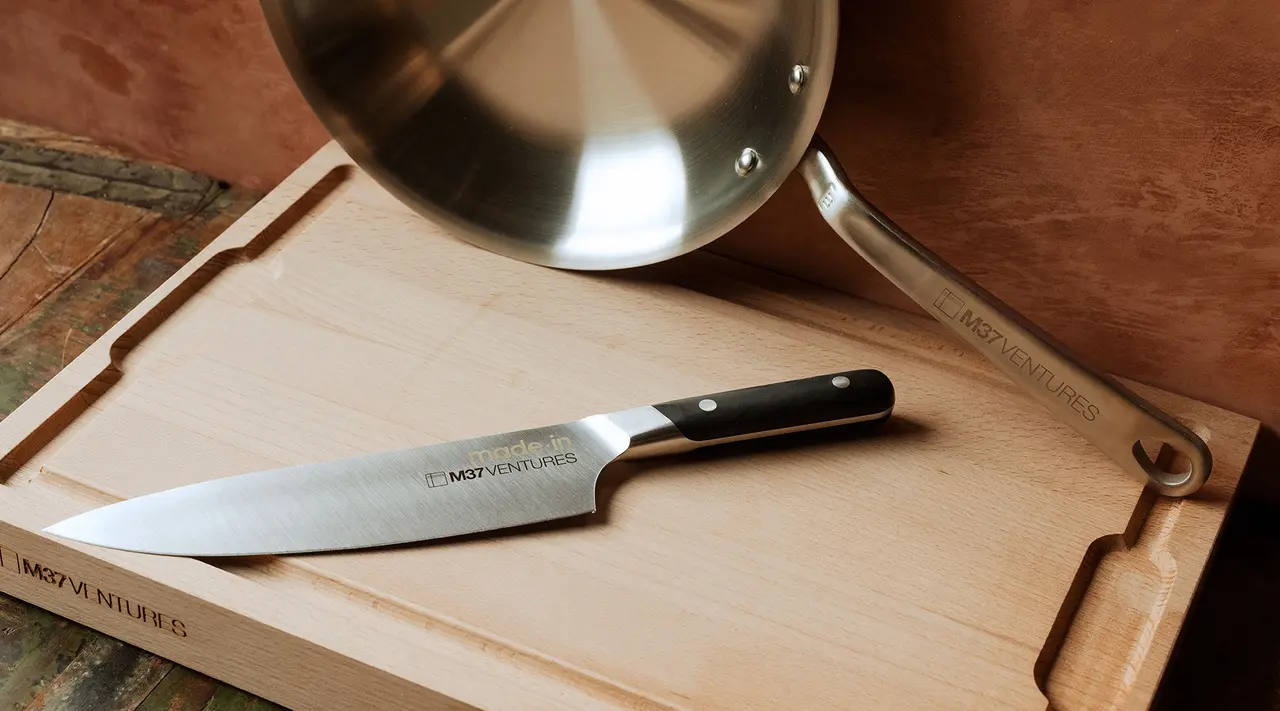 A chef's knife and a stainless steel saucepan are positioned on a wooden cutting board, showcasing kitchen essentials.