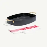 A black oval grill pan with gold handles is displayed next to a white towel featuring a red "MADE" lettering.
