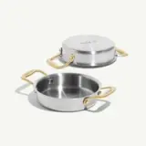 A stainless steel cookware piece with gold handles, featuring a lid and an open vessel.