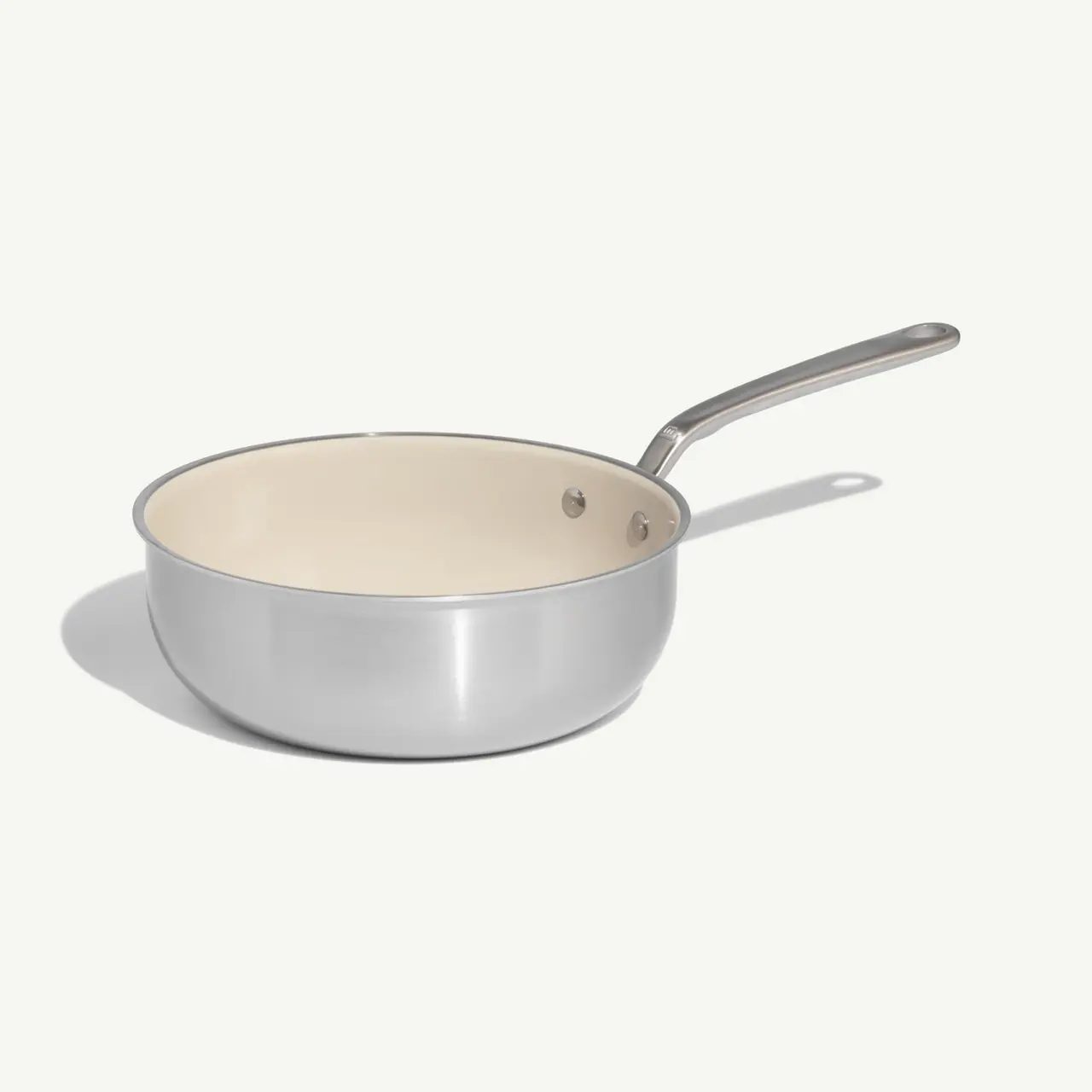 A stainless steel frying pan with a cream-colored non-stick interior and a long handle.