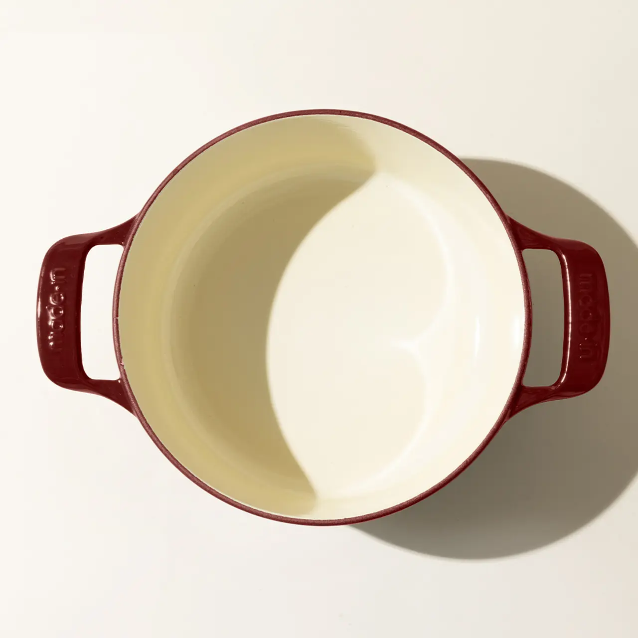 An empty round red ceramic Dutch oven with side handles and a cream interior viewed from above.