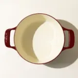 An empty round red ceramic Dutch oven with side handles and a cream interior viewed from above.