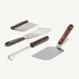 Four stainless steel cooking utensils with wooden handles, including a spatula, grill fork, dough cutter, and a slotted turner, arranged neatly.