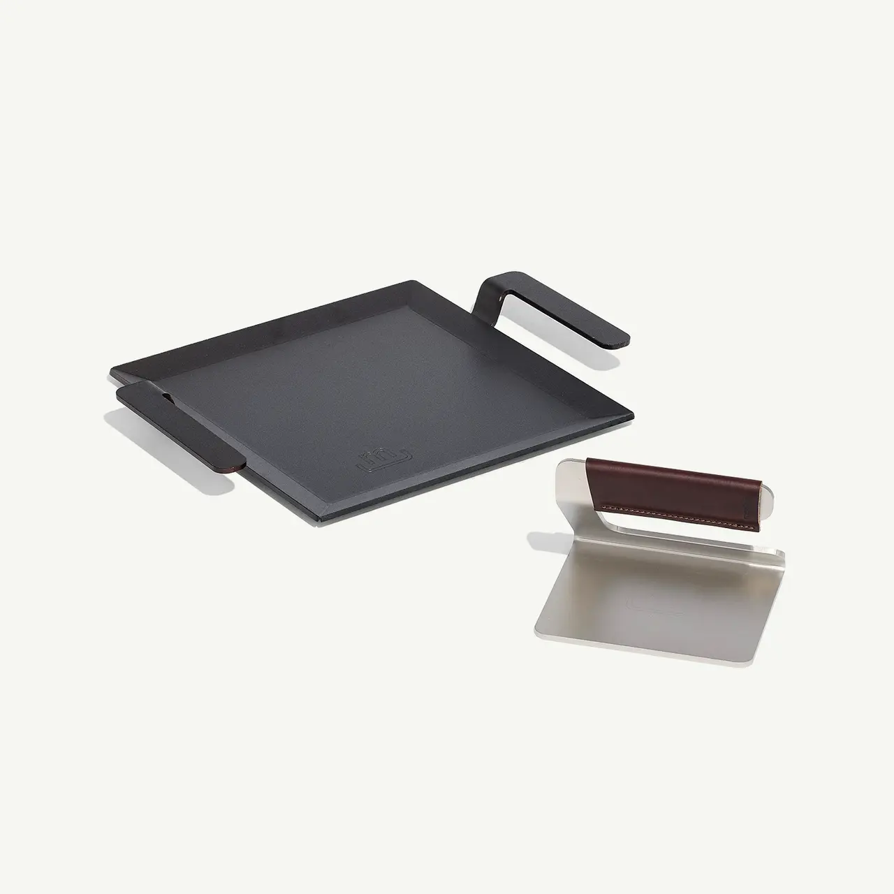 A black griddle pan and a white and brown squeegee on a light background.