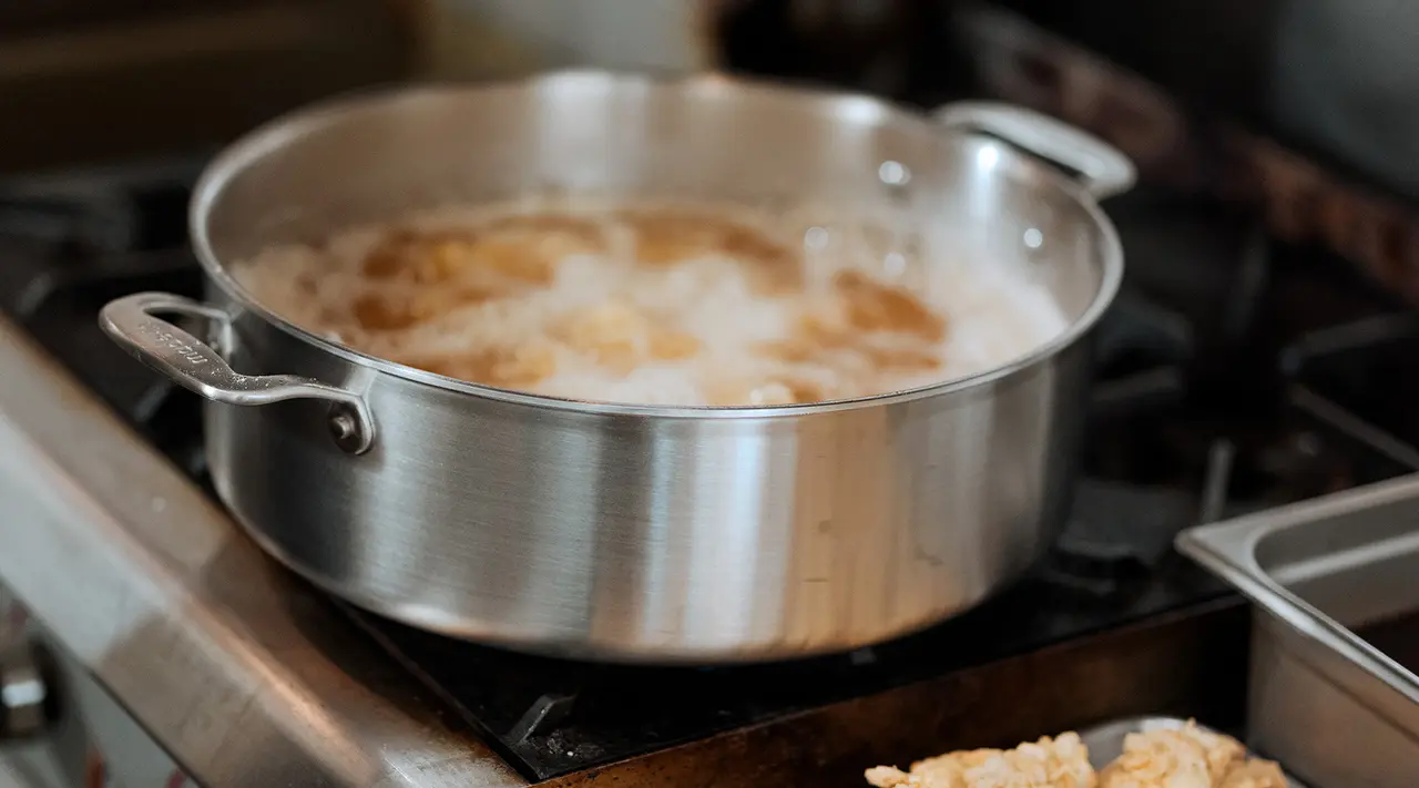 A stainless steel pot simmers on a stove with food cooking inside.