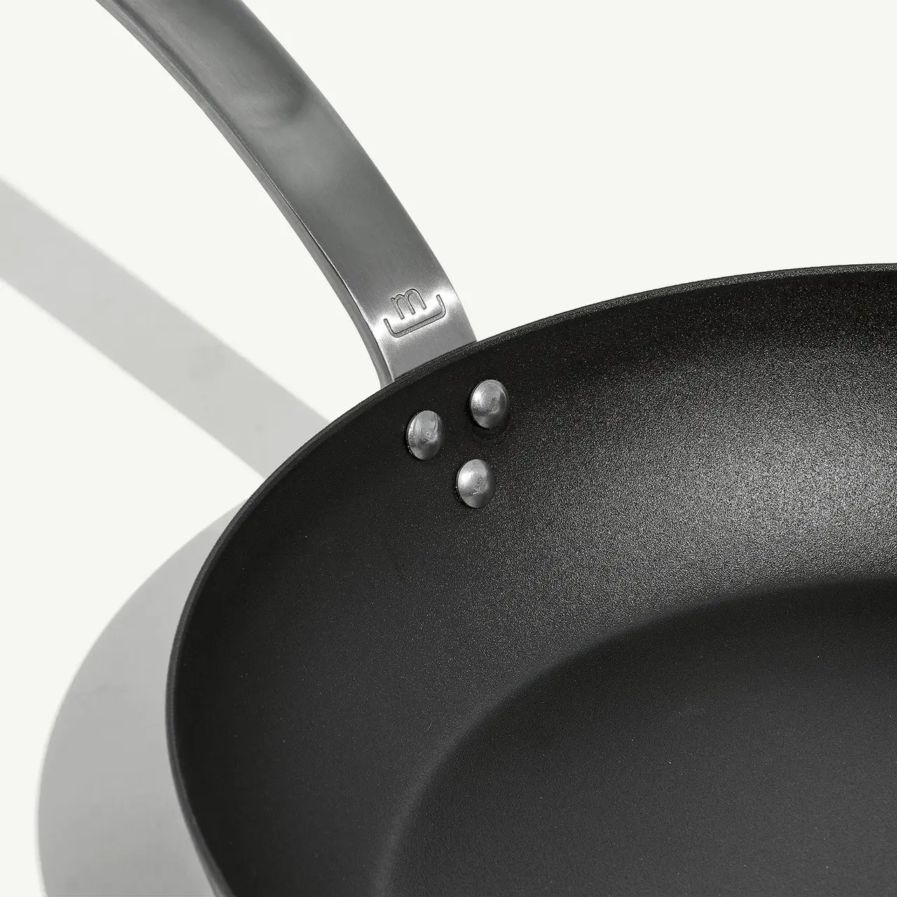 A non-stick frying pan is shown at a slight angle, displaying its interior surface and part of the handle against a light background with subtle shadows.