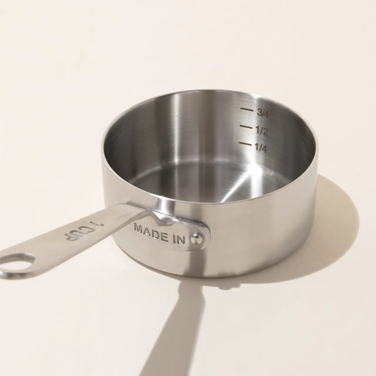 A stainless steel measuring cup with volume markings inside sits on a surface casting a soft shadow.