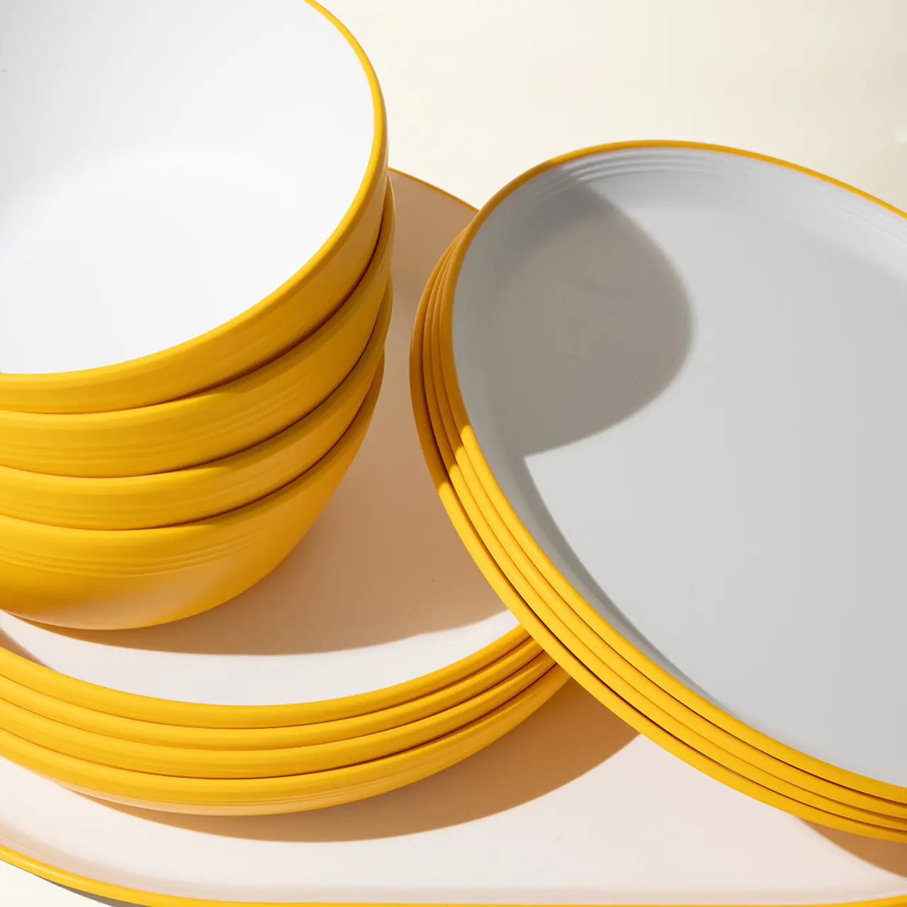 Stacks of yellow-edged plates are neatly arranged on a table, casting soft shadows in the light.