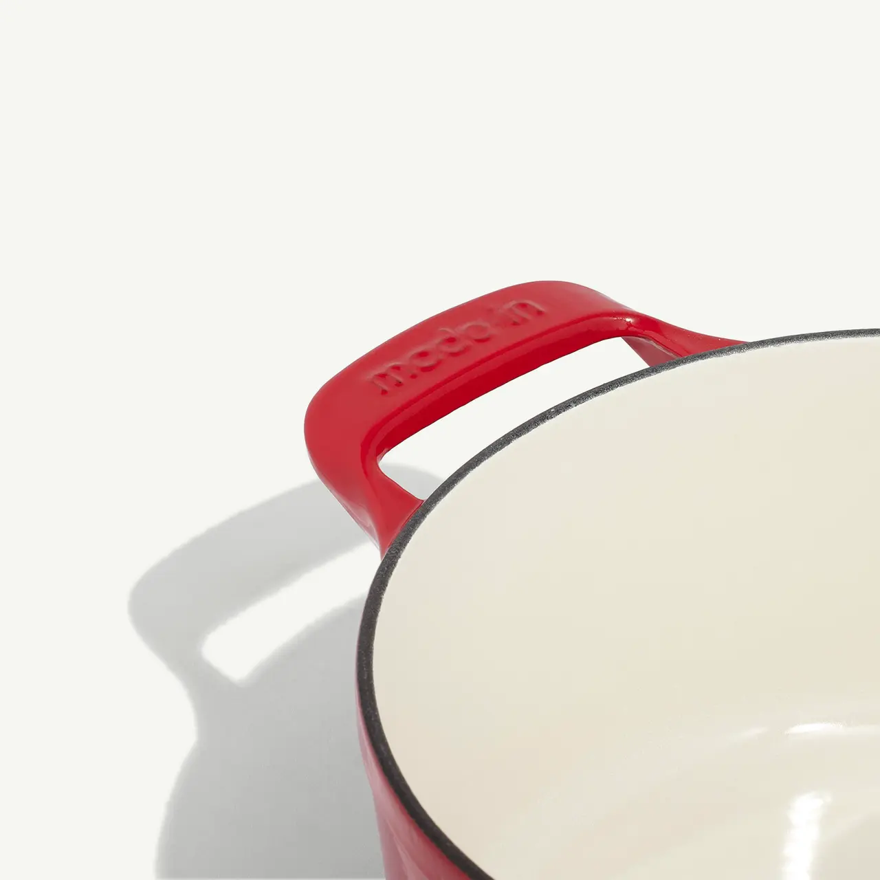 A red enameled pot with a visible logo on the handle casts a shadow on a light background.
