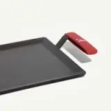 A flat griddle with a red handle and a small spatula attachment.