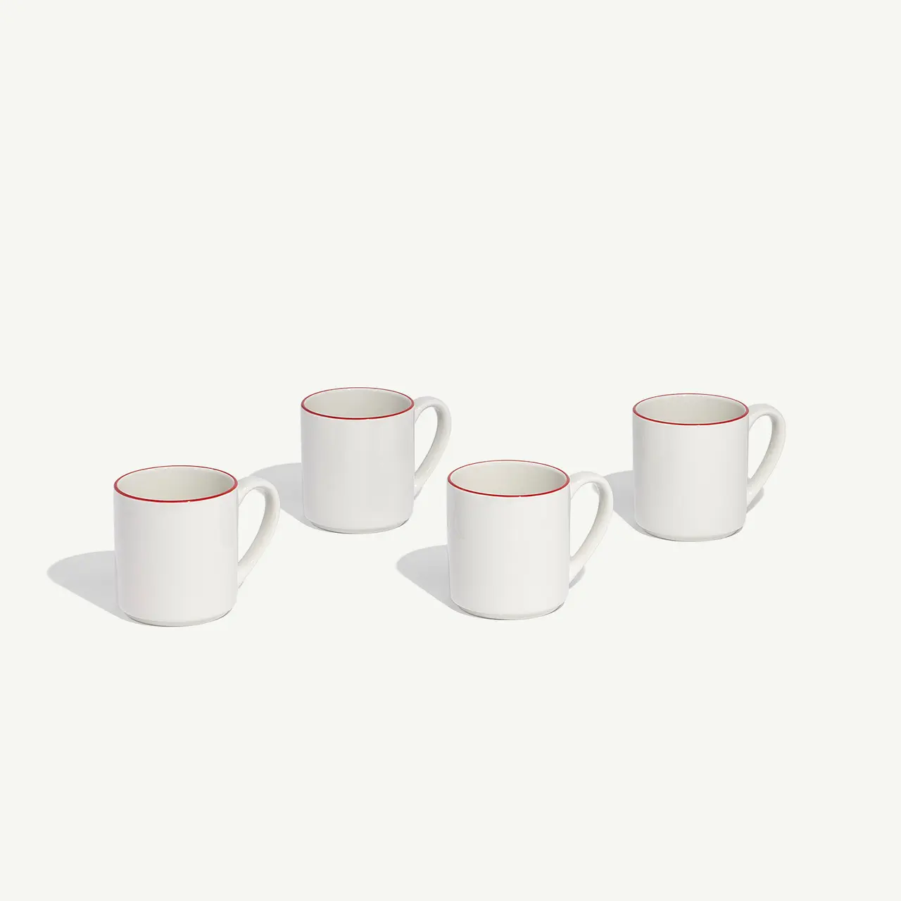 Four white mugs with red rims are arranged in a line on a light background.
