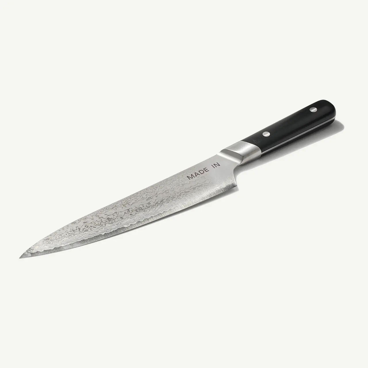 A chef's knife with a patterned steel blade and a black handle lies against a white background.