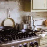 A modern kitchen countertop features various pots and pans, including frying pans and a stockpot, arranged neatly near a stove.