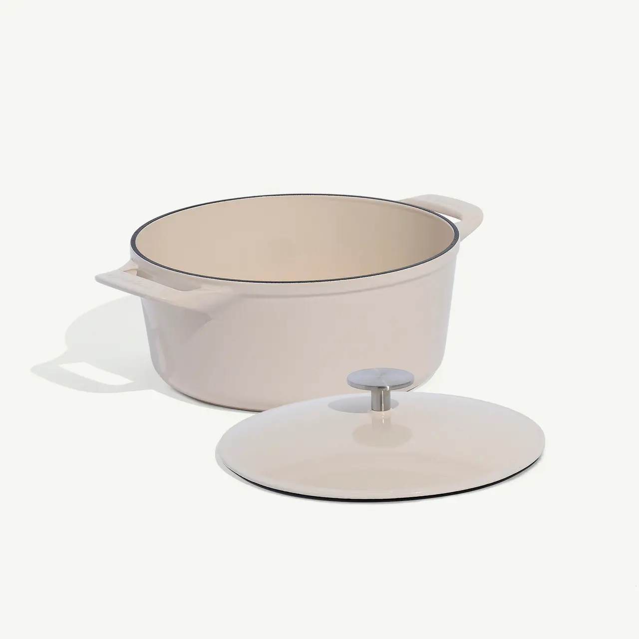 A beige cooking pot with handles and a lid off to the side on a white background.