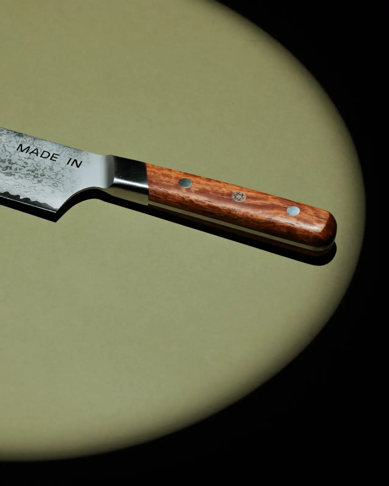 A wooden-handled pocket knife lies on a tan oval background, casting a slight shadow.