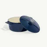 A dark blue enameled cast iron Dutch oven with its lid slightly askew, displayed on a plain background.