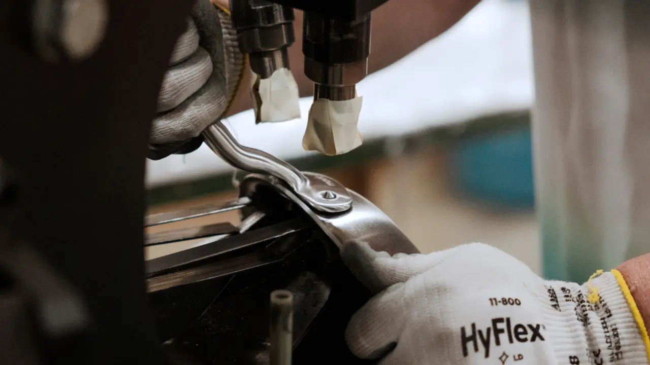 A worker in gloves operates a machine to manipulate a metal component in a manufacturing setting.