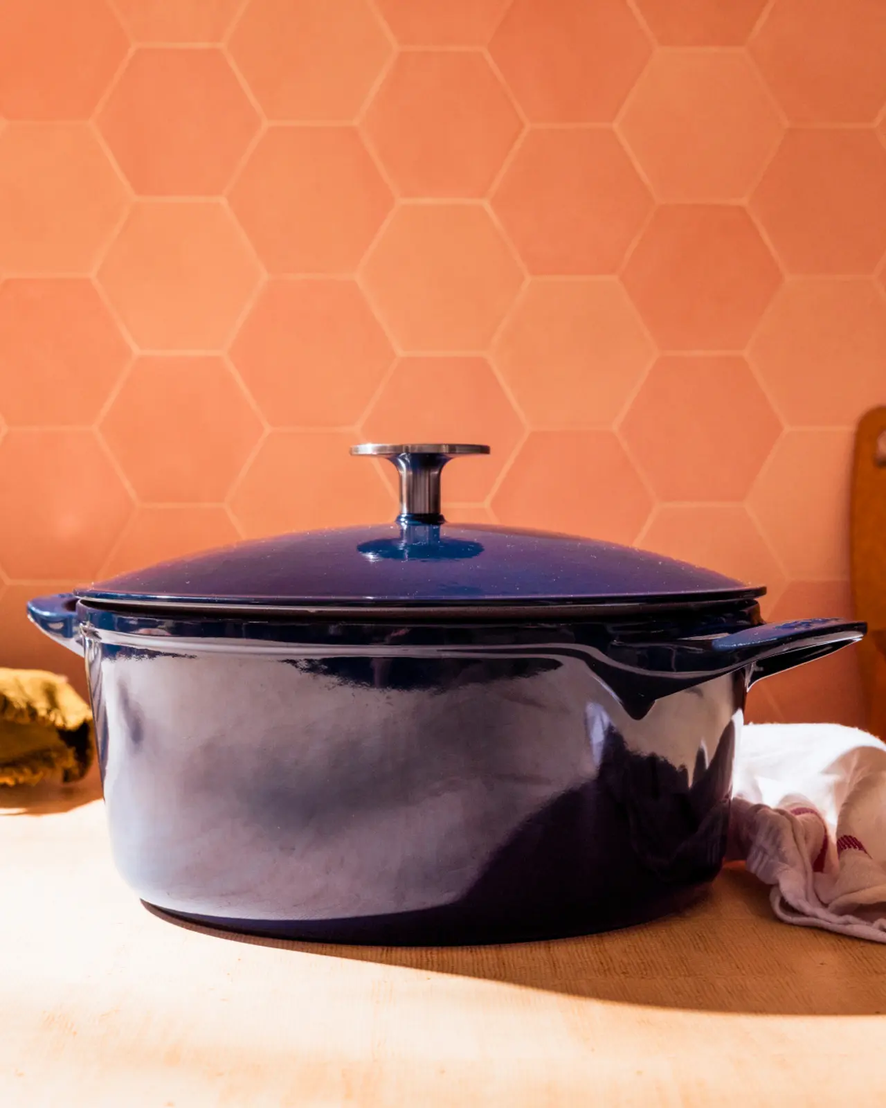 A shiny blue cast iron pot sits on a countertop against a backdrop of orange hexagonal tiles.