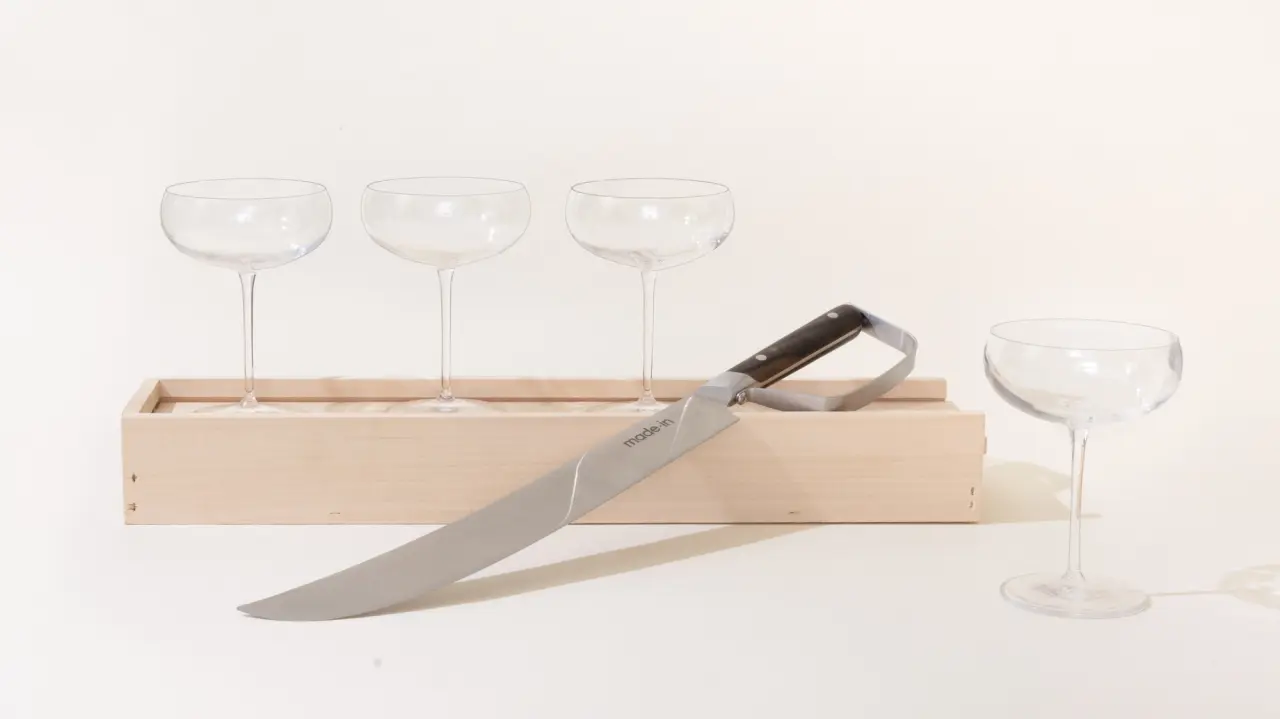 Three empty wine glasses stand next to a wooden box, with a large chef's knife partially covering the box, against a light background.