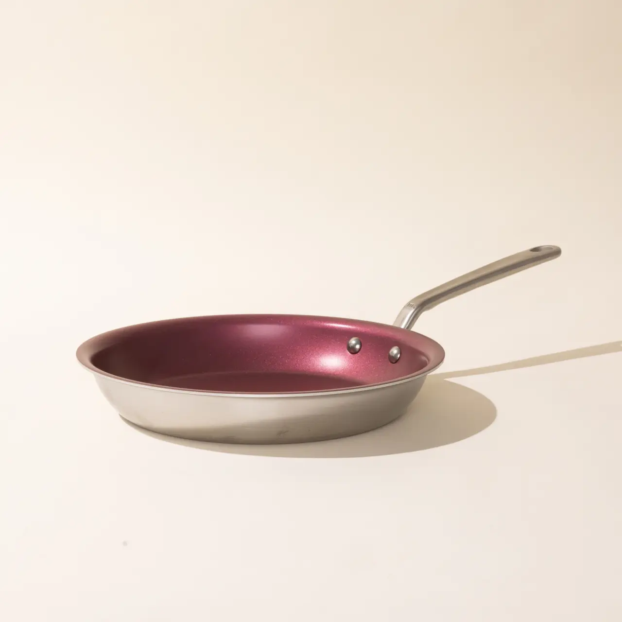 A pink non-stick frying pan with a silver handle on a pale background, casting a soft shadow.