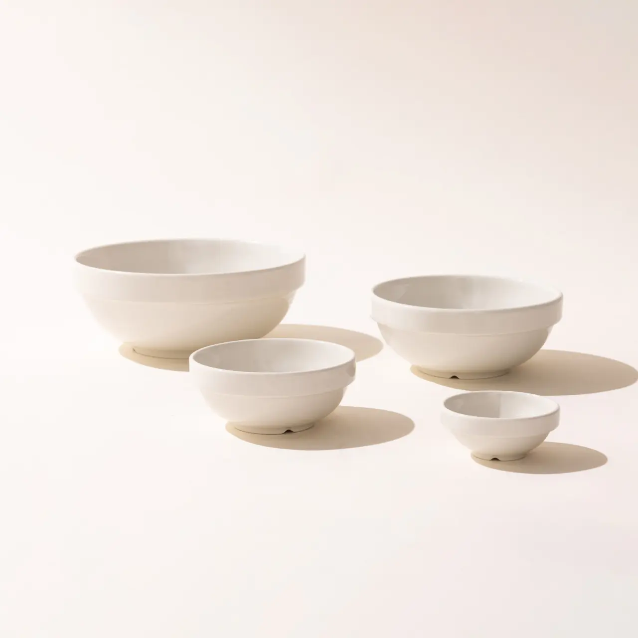 Four white bowls of varying sizes are arranged in a descending order on a light background.