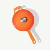 A bright orange frying pan with a lid is shown against a light background.