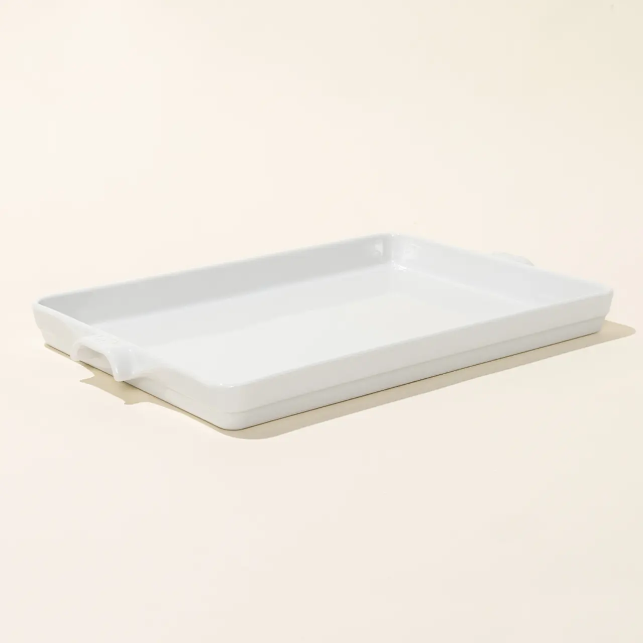 A simple white ceramic baking dish is featured on a light beige background.