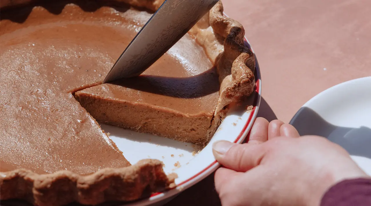 A person is slicing a pumpkin pie and serving a piece onto a plate.