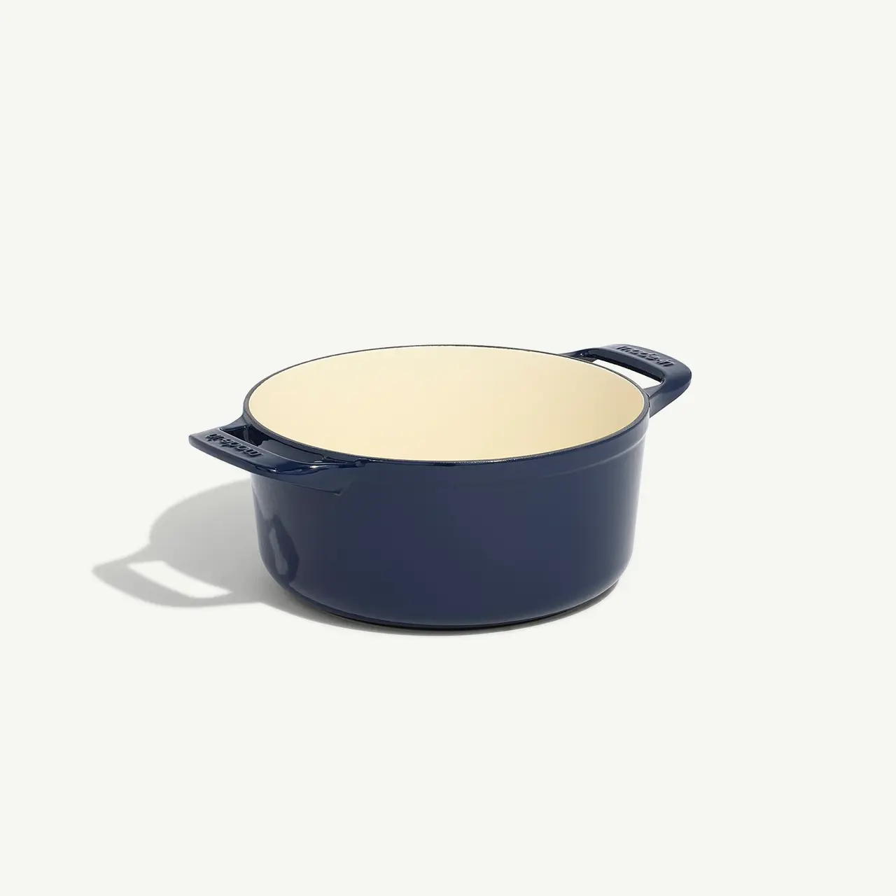 A navy blue enameled cast iron Dutch oven sits on a light background.