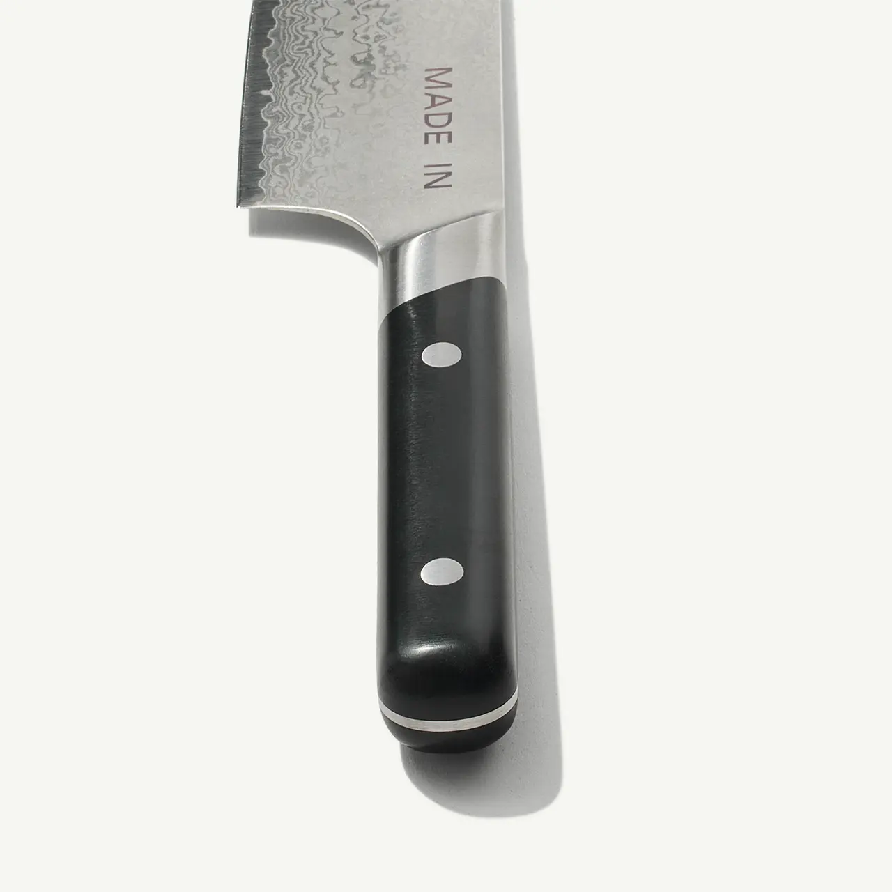 A close-up of a kitchen knife with a serrated blade and a black handle against a white background.