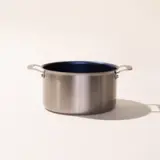 A stainless steel pot with two handles and a dark interior sits on a neutral background, casting a soft shadow.