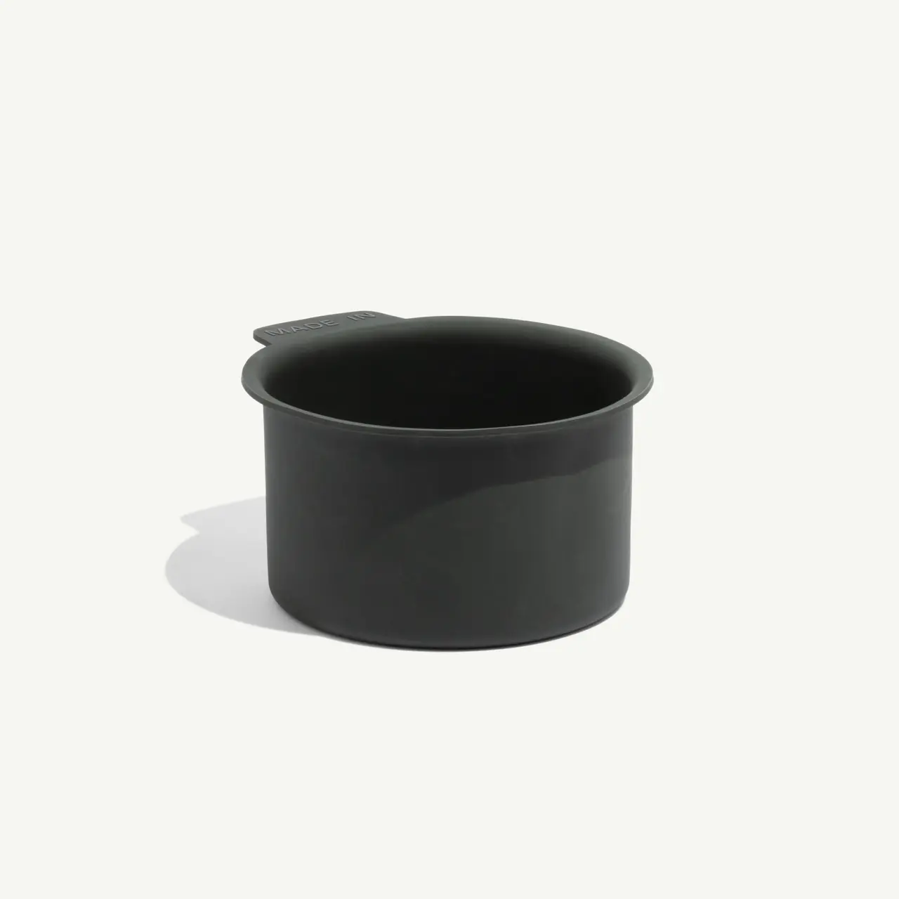 A dark green, round container with a handle and a smooth finish sits on a light background.