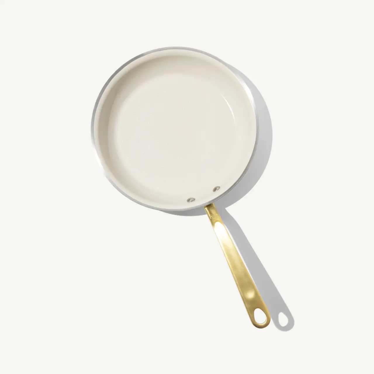 A white frying pan with a gold handle is displayed on a light background.