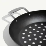 A black frying pan with a perforated surface and sturdy handles.