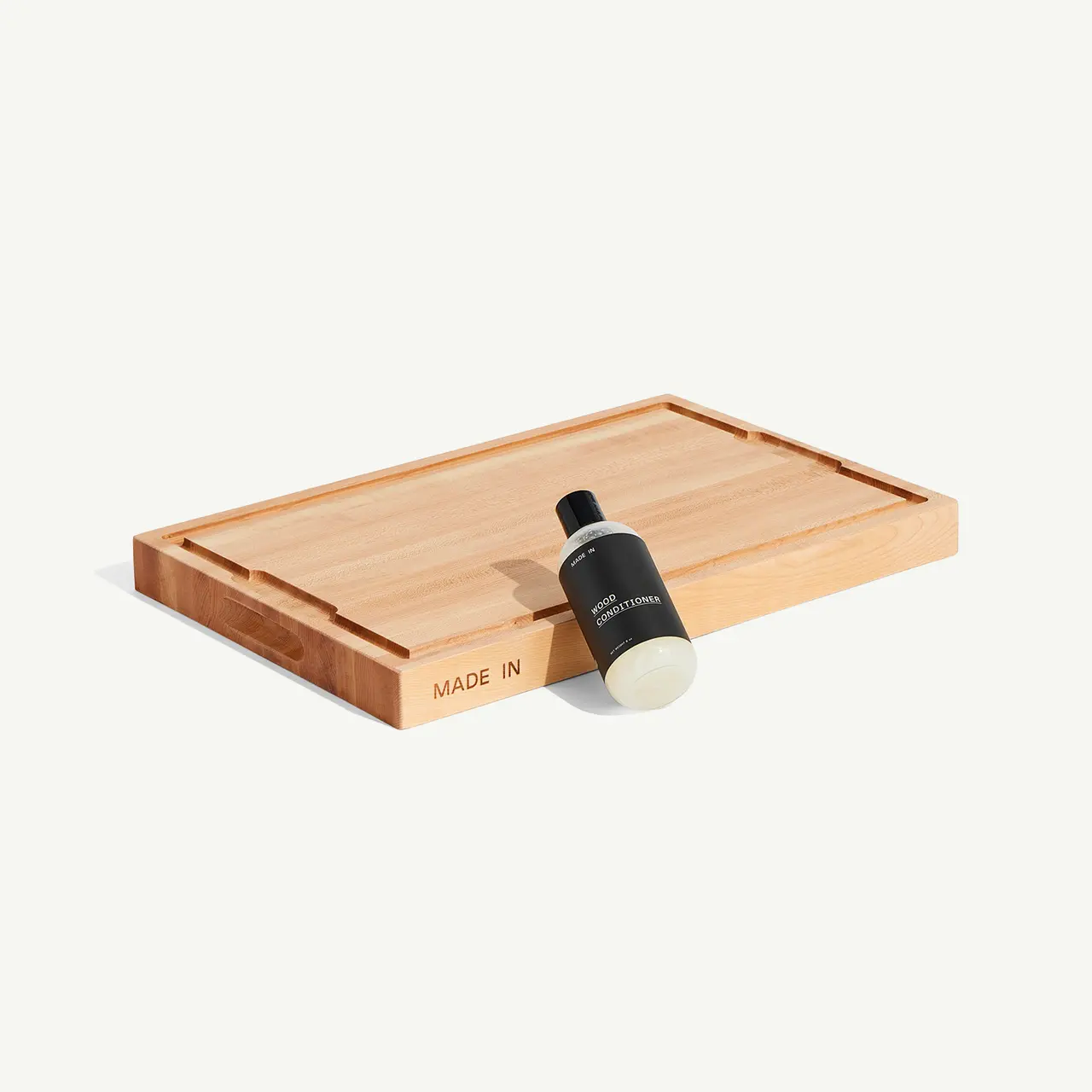 A wooden tray holds a bottle with a black label next to a small, round object on a minimalist background.