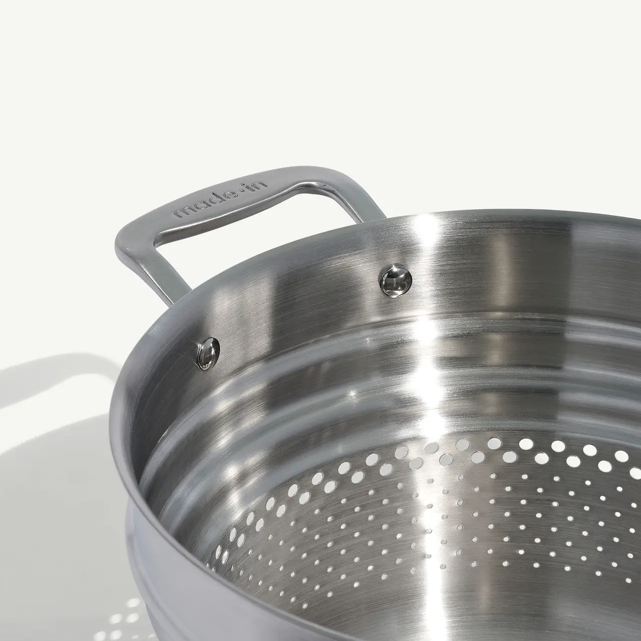 A stainless steel colander with a handle is shown against a white background.