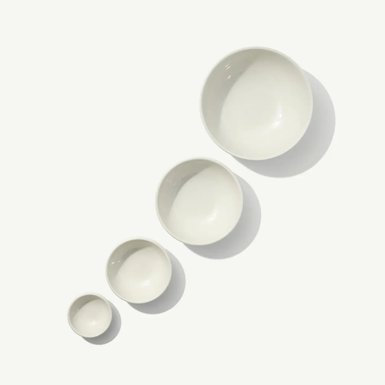 Four white bowls of varying sizes are arranged in ascending order on a pale surface.