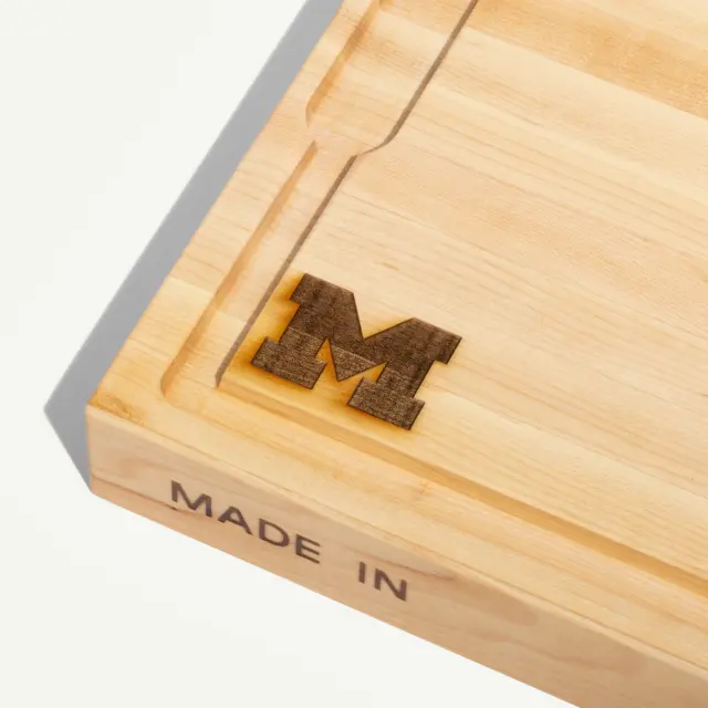 A wooden tray features a raised letter "M" on one side and the words "MADE IN" engraved on the opposite side.