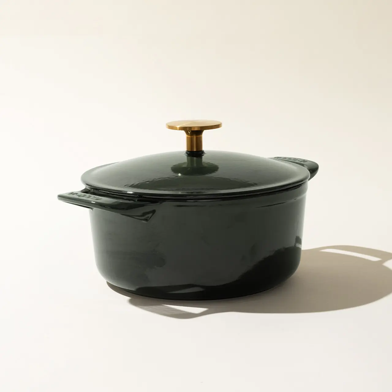 A green enameled cast iron Dutch oven with a gold-colored knob on its lid, set against a light background.