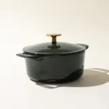 A green enameled cast iron Dutch oven with a gold-colored knob on its lid, set against a light background.