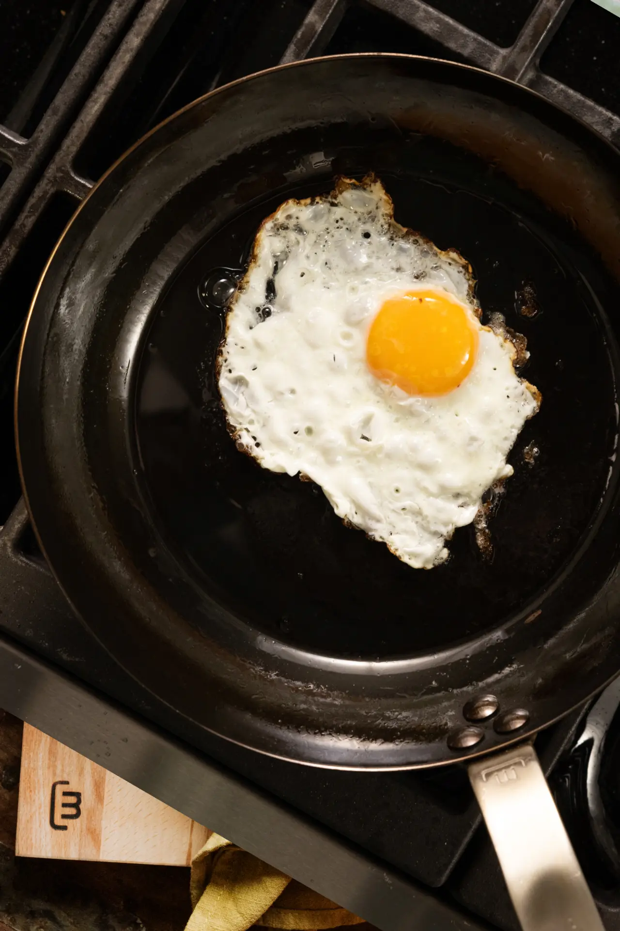 A single fried egg with a bright yellow yolk is sizzling in a black skillet on a stovetop.