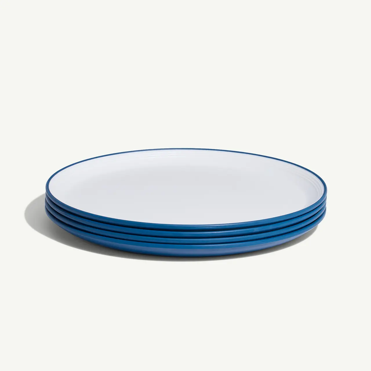 A stack of clean white plates with blue rims on a neutral background.