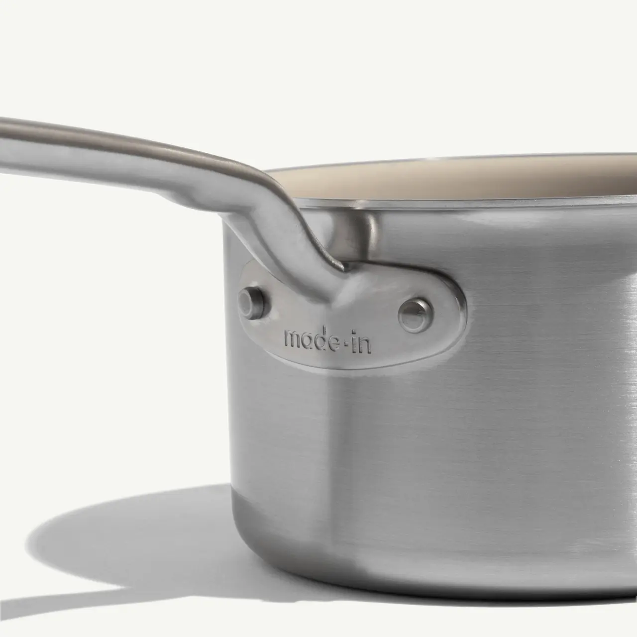 A stainless steel saucepan with a long handle features the engraving "made-in" on its side.