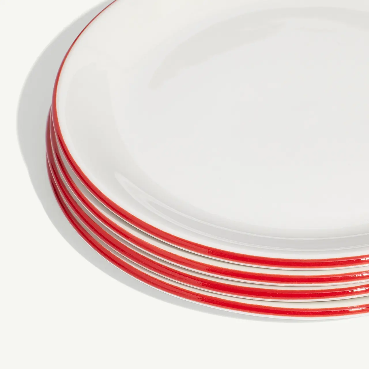 A stack of white plates with red trim on a light background.