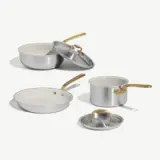 Four cookware pieces, including two frying pans, a pot with a lid, and a saucepan, featuring sleek silver surfaces and gold handles.