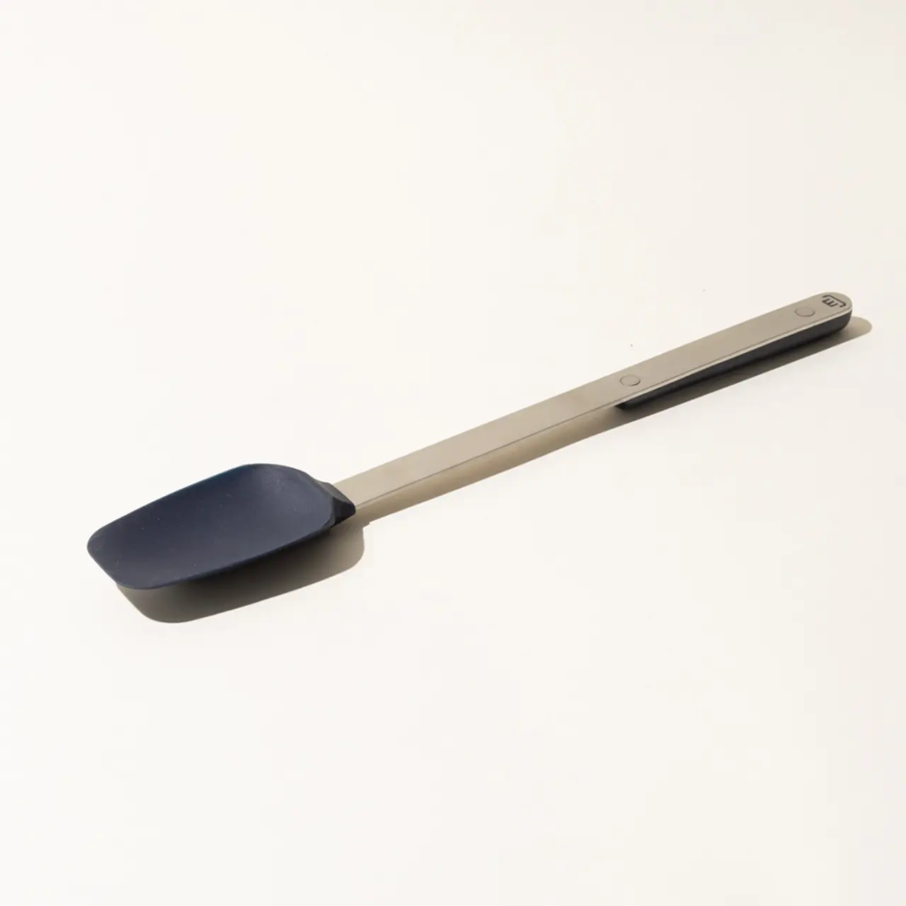 A silicone spatula with a long metal handle lies on a plain white surface.