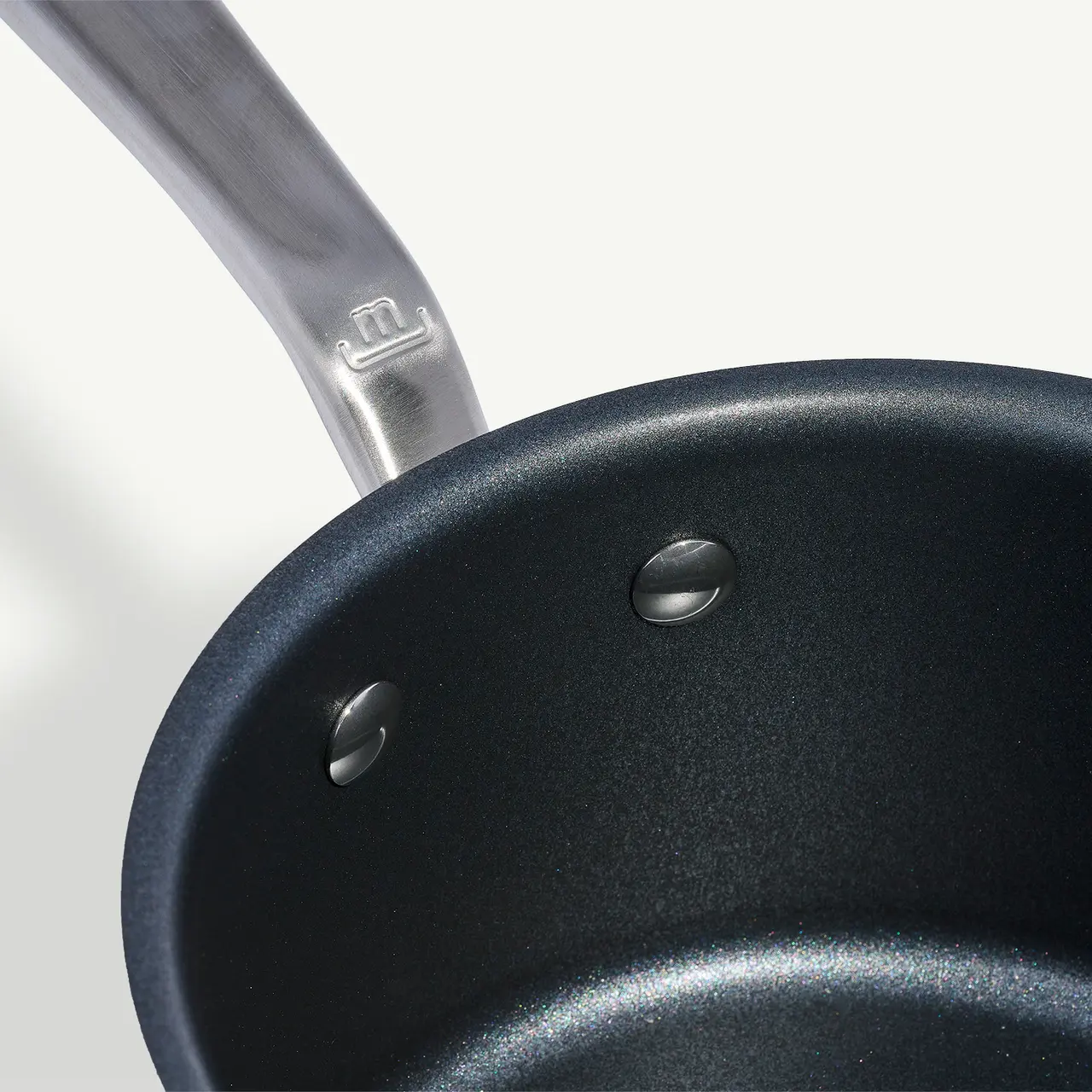 A close-up view of a non-stick frying pan with two water droplets inside and a visible section of its handle.