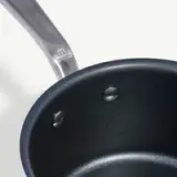 A close-up view of a non-stick frying pan with two water droplets inside and a visible section of its handle.